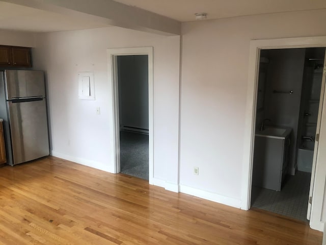 unfurnished bedroom with a baseboard heating unit, ensuite bath, a spacious closet, light hardwood / wood-style floors, and stainless steel refrigerator