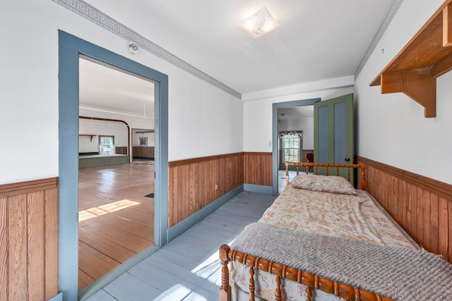 bedroom featuring wood walls, light hardwood / wood-style floors, crown molding, and multiple windows