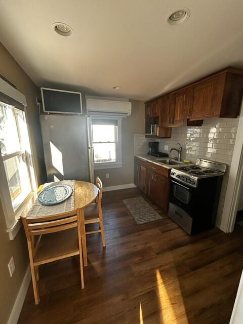 kitchen featuring decorative backsplash, dark hardwood / wood-style flooring, gas range, sink, and an AC wall unit