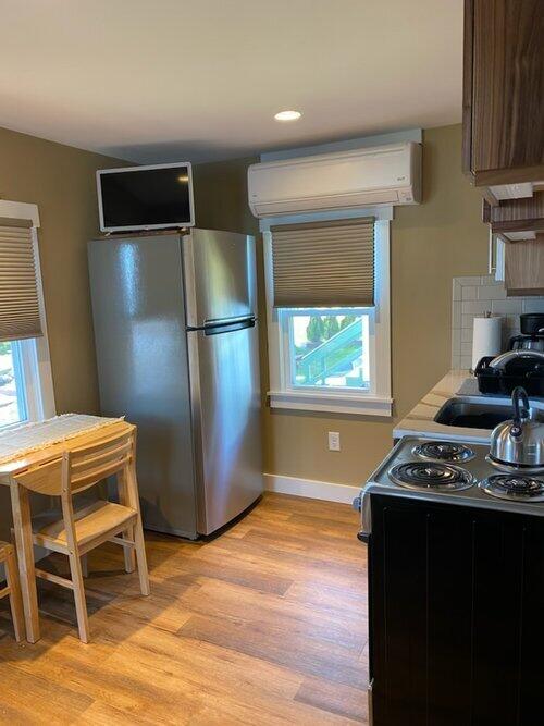 kitchen featuring electric range, stainless steel fridge, a wall unit AC, and light hardwood / wood-style flooring