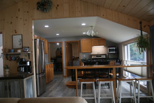 kitchen featuring stainless steel appliances, light hardwood / wood-style flooring, vaulted ceiling, wooden walls, and wood ceiling