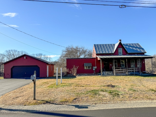 view of front of house featuring a garage, covered porch, an outbuilding, and a front lawn