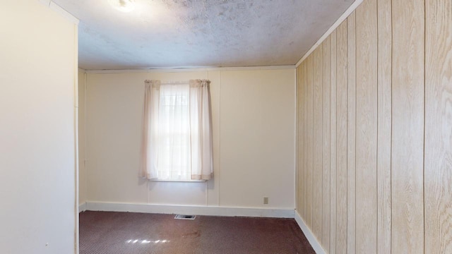 carpeted empty room featuring wood walls