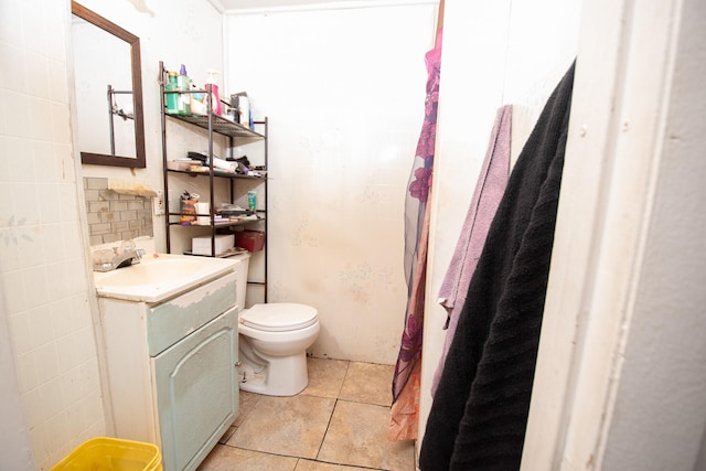 bathroom featuring toilet, vanity, tile patterned floors, and tile walls