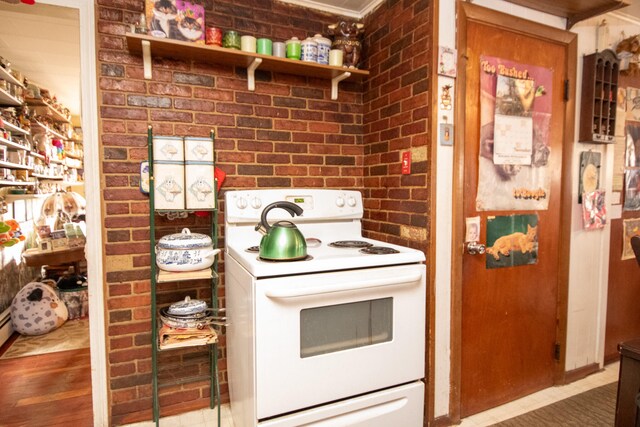 kitchen with brick wall, hardwood / wood-style flooring, crown molding, and electric stove