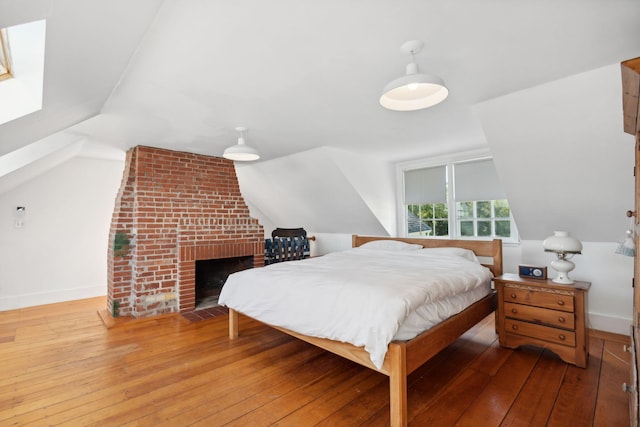 bedroom featuring a fireplace, lofted ceiling, and hardwood / wood-style flooring