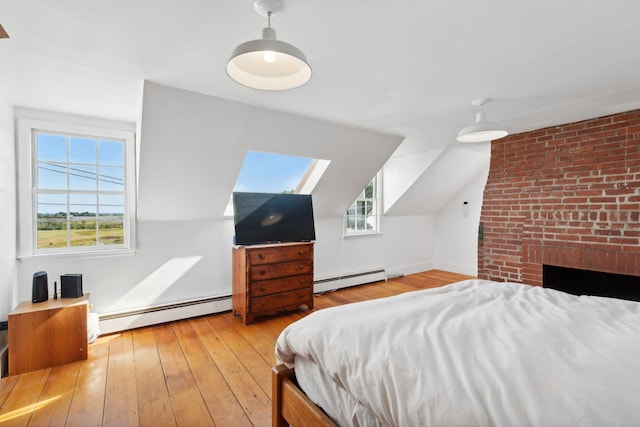 bedroom with lofted ceiling with skylight, light wood-type flooring, and a baseboard heating unit