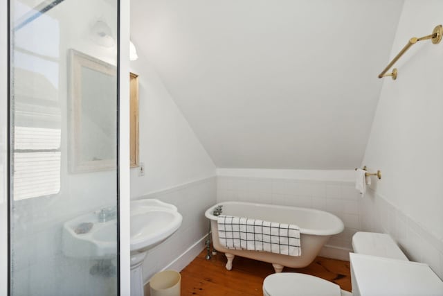 bathroom featuring a bathing tub, wood-type flooring, lofted ceiling, toilet, and tile walls