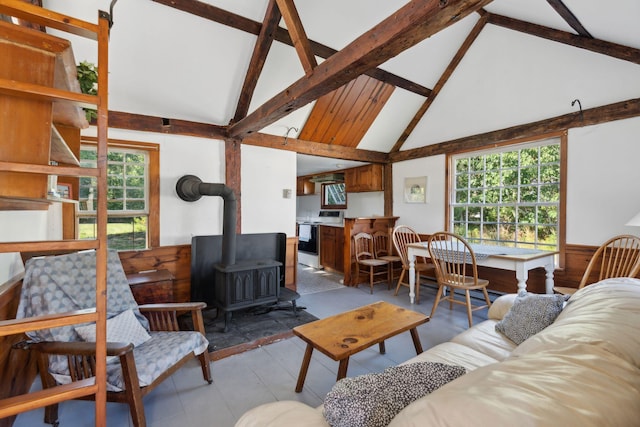 living room with plenty of natural light, beam ceiling, a wood stove, and high vaulted ceiling