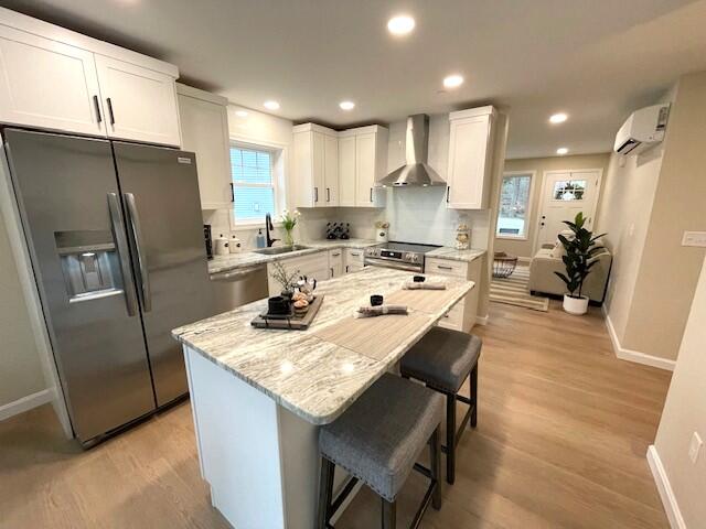 kitchen featuring white cabinets, appliances with stainless steel finishes, plenty of natural light, and wall chimney exhaust hood