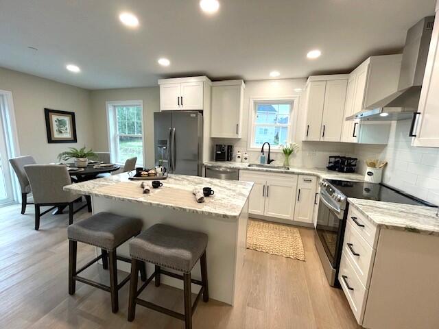 kitchen featuring wall chimney exhaust hood, a center island, white cabinetry, and appliances with stainless steel finishes