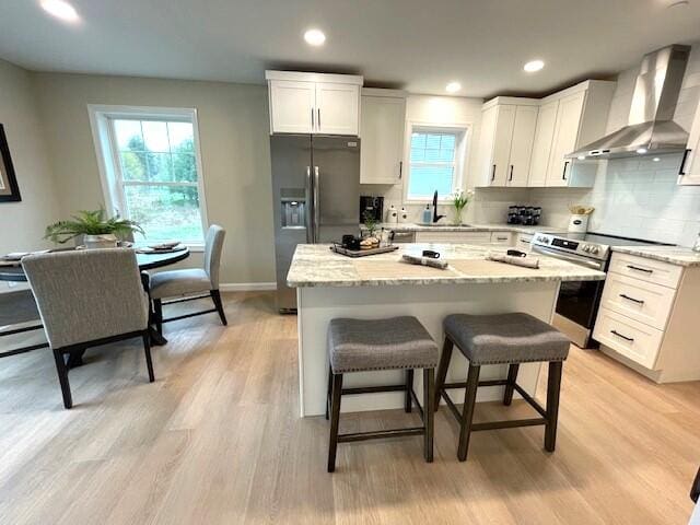 kitchen featuring white cabinetry, light stone countertops, wall chimney range hood, and appliances with stainless steel finishes