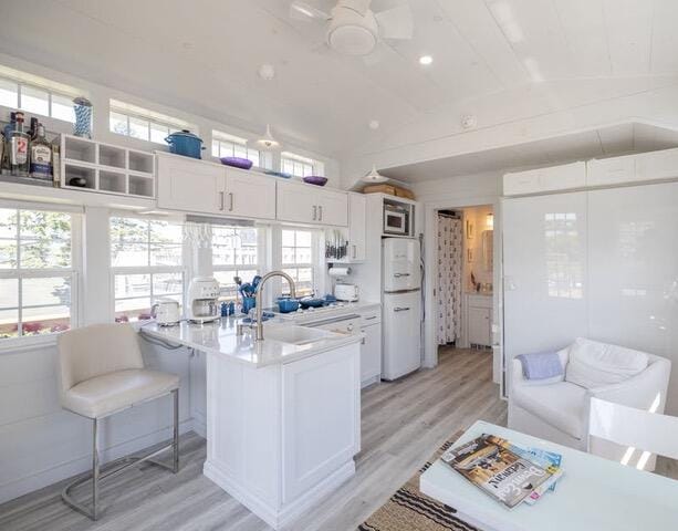 kitchen featuring white cabinetry, light countertops, freestanding refrigerator, light wood finished floors, and stainless steel microwave