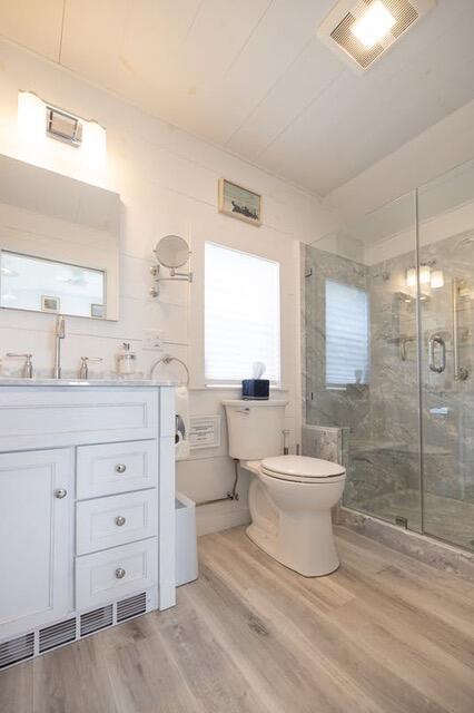 full bathroom featuring visible vents, toilet, wood finished floors, vanity, and a shower stall