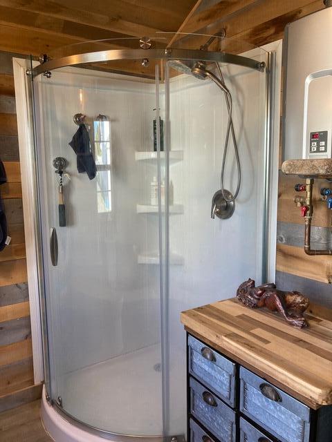 full bathroom with water heater, wood walls, and a stall shower