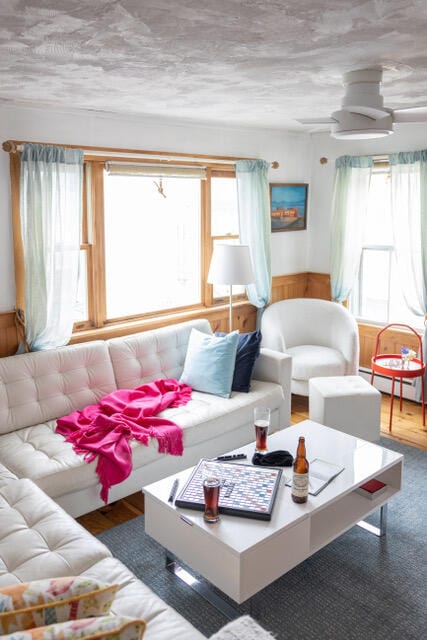 living room featuring a baseboard heating unit, wainscoting, and ceiling fan