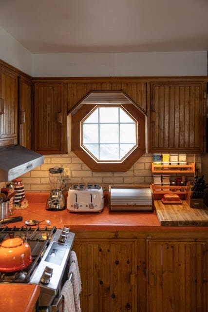 kitchen featuring tasteful backsplash, range hood, brown cabinets, and stainless steel gas stove