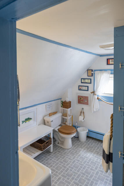 interior space with toilet, brick floor, a baseboard heating unit, and lofted ceiling