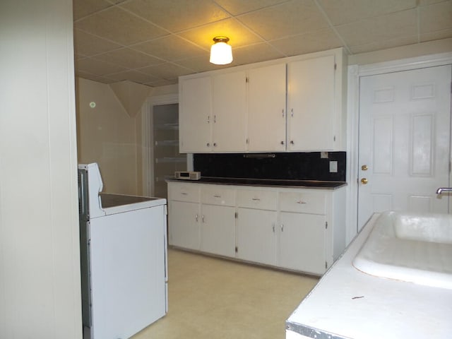 kitchen featuring a paneled ceiling, stove, sink, tasteful backsplash, and white cabinetry