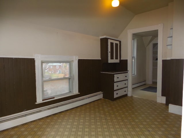 empty room featuring baseboard heating, wooden walls, and lofted ceiling