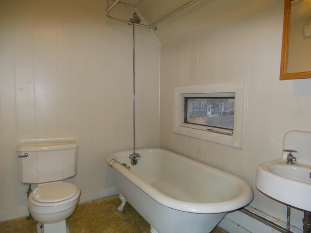 bathroom with a tub to relax in, wood walls, sink, and toilet