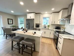 kitchen featuring stainless steel electric range, a kitchen island, white cabinetry, and black refrigerator with ice dispenser