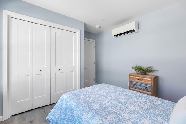 bedroom with a closet, wood finished floors, and a wall mounted air conditioner