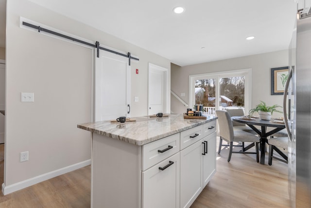 kitchen with light wood-type flooring, a barn door, light stone counters, and white cabinets