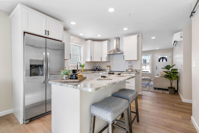 kitchen with decorative backsplash, a wall mounted AC, wall chimney range hood, stainless steel fridge, and plenty of natural light