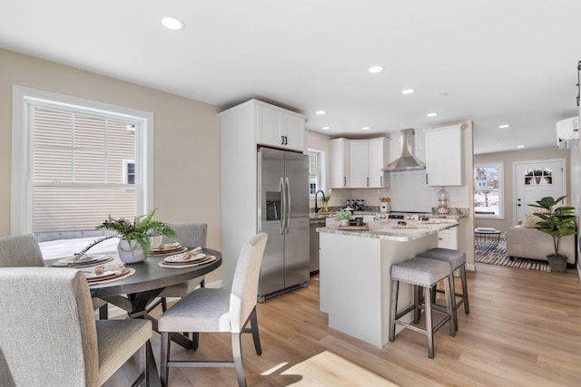 kitchen featuring tasteful backsplash, appliances with stainless steel finishes, a breakfast bar area, a center island, and wall chimney range hood