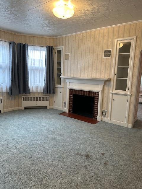 unfurnished living room featuring carpet flooring, radiator heating unit, and a brick fireplace