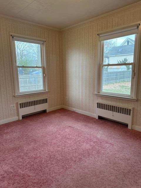 carpeted spare room featuring radiator heating unit, crown molding, and a wealth of natural light