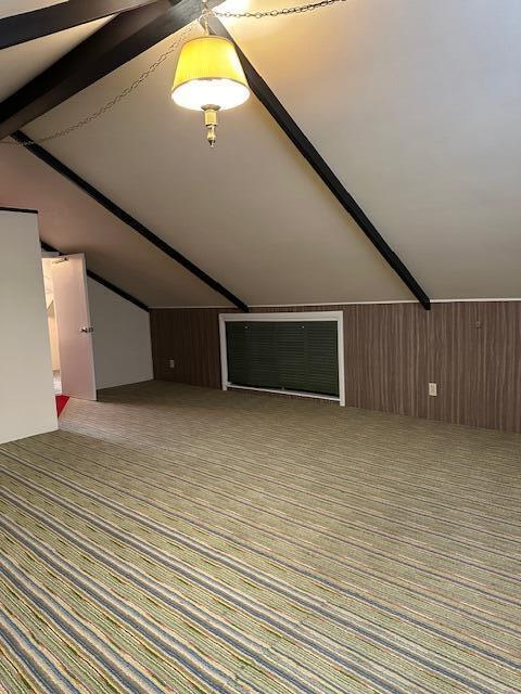 bonus room with carpet, lofted ceiling with beams, and wooden walls