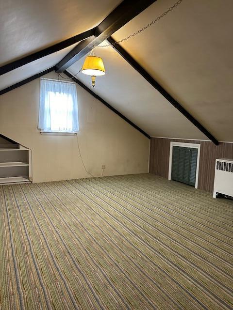 additional living space featuring wooden walls, lofted ceiling with beams, carpet floors, and radiator