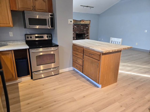 kitchen with track lighting, light wood-type flooring, a fireplace, kitchen peninsula, and stainless steel appliances