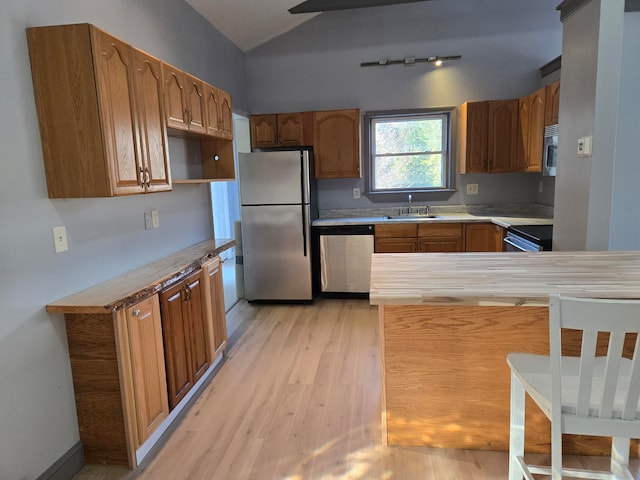 kitchen with lofted ceiling, sink, light wood-type flooring, appliances with stainless steel finishes, and kitchen peninsula