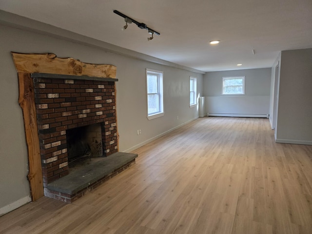 unfurnished living room featuring a fireplace, light wood-type flooring, plenty of natural light, and a baseboard heating unit