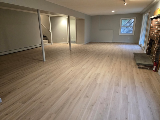 basement featuring baseboard heating, light hardwood / wood-style flooring, and a brick fireplace