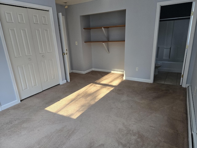 unfurnished bedroom featuring ensuite bathroom, a closet, light colored carpet, and a baseboard heating unit