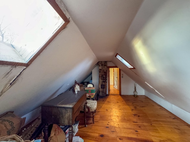 additional living space with lofted ceiling with skylight and light hardwood / wood-style flooring