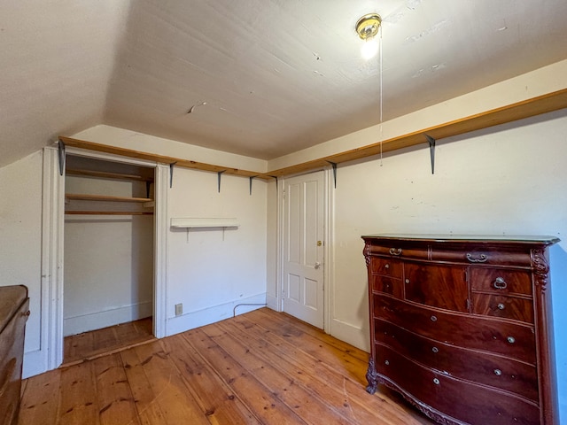 unfurnished bedroom featuring light hardwood / wood-style floors, vaulted ceiling, and a closet