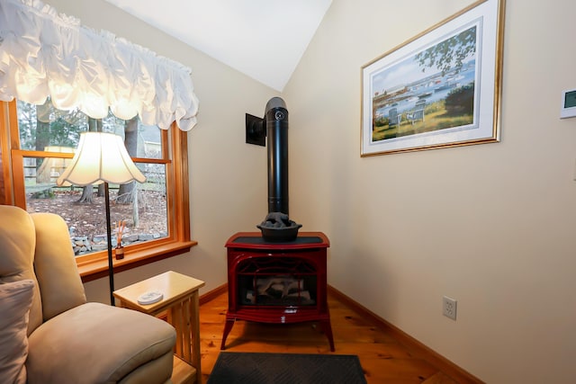 living area with a wood stove, hardwood / wood-style flooring, and vaulted ceiling