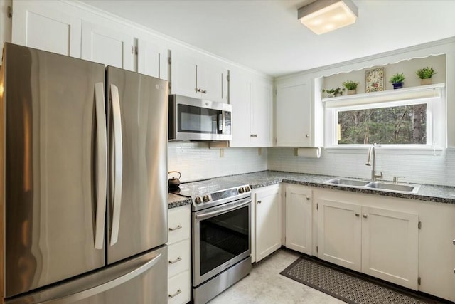 kitchen with appliances with stainless steel finishes, tasteful backsplash, sink, dark stone countertops, and white cabinetry