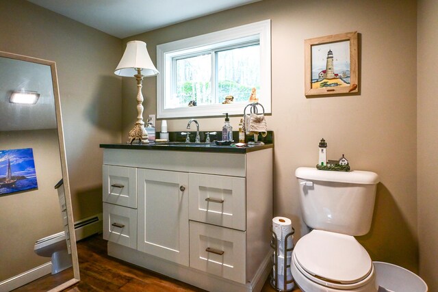 half bathroom featuring toilet, wood finished floors, vanity, baseboards, and baseboard heating