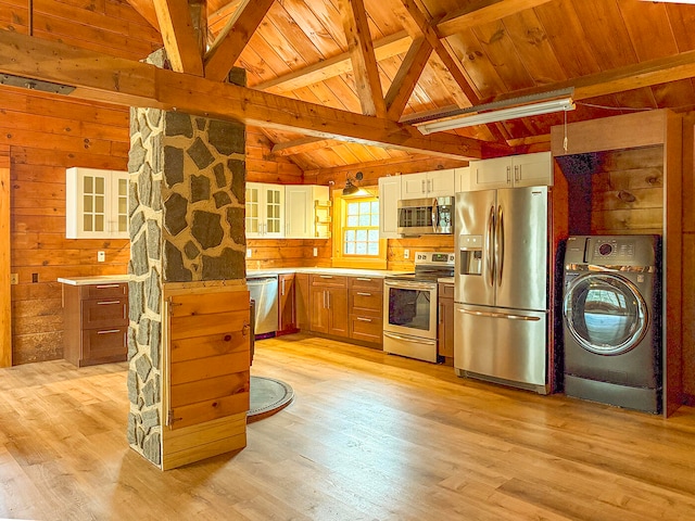 kitchen featuring hanging light fixtures, wooden walls, light hardwood / wood-style flooring, appliances with stainless steel finishes, and washer / clothes dryer