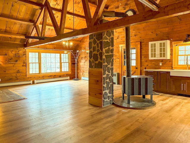 unfurnished living room with a baseboard heating unit, wooden ceiling, light hardwood / wood-style floors, a wood stove, and wood walls