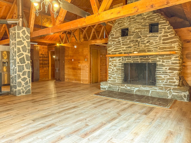 unfurnished living room featuring wood-type flooring, beam ceiling, high vaulted ceiling, a stone fireplace, and wood walls