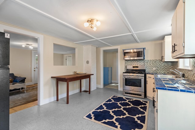 kitchen featuring sink, appliances with stainless steel finishes, tasteful backsplash, tile counters, and white cabinetry