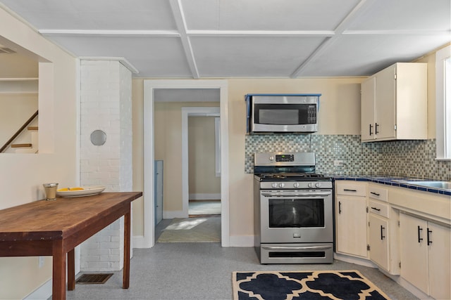 kitchen with tile counters, backsplash, appliances with stainless steel finishes, and cream cabinets