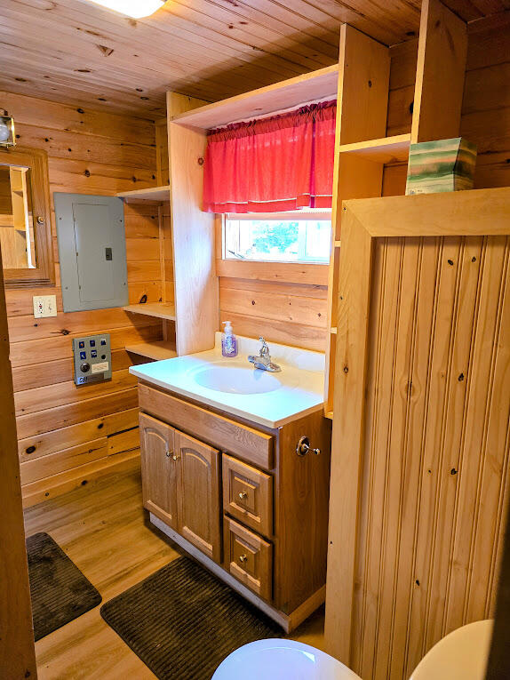 bathroom featuring vanity, hardwood / wood-style flooring, wooden ceiling, electric panel, and wood walls